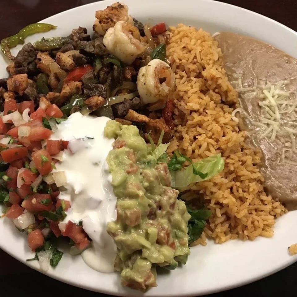 Mexican mixed platter with grilled meat, shrimp, rice, beans, pico de gallo, sour cream, guacamole, and lettuce.